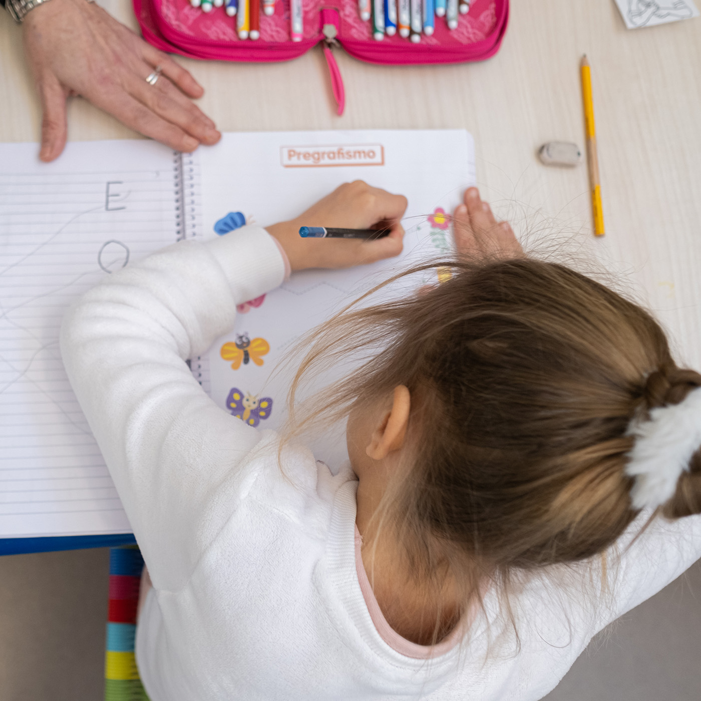 Bambina vista dall'alto mentre scrive su un quaderno · Lega del Filo d'Oro