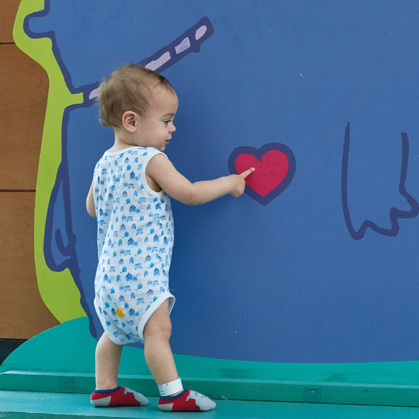 Bambino piccolo tocca un cuore disegnato su un muro colorato · Fondazione Meyer